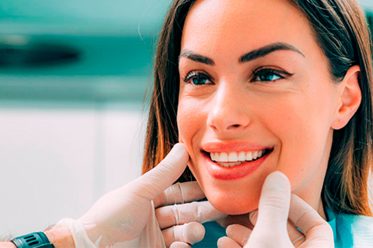 Un especialista comprueba el resultado del tratamiento de estética dental que ha recibido una paciente.